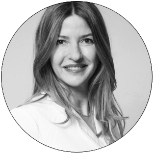 Retrato en blanco y negro de una mujer con cabello largo y lacio, sonriendo y vestida con una blusa blanca.